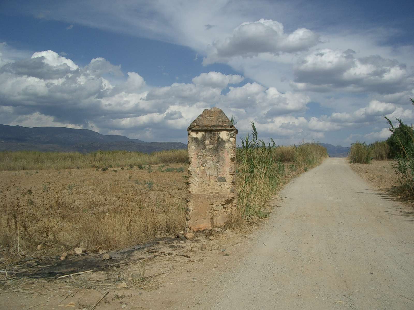 Short stone pillar with tapered top, to the left of a road and to the right of a field