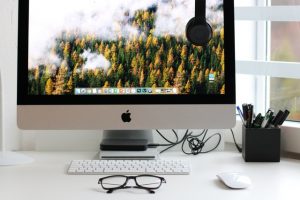 iMac, mouse, keyboard, and a pair of glasses on a white desk