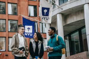 Three students in front of NYU (New York University) flags