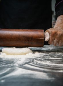 Baker using a rolling pin on dough.