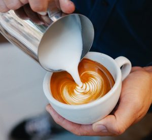 Barista pouring milk into a cappuccino.