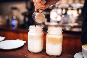 White coffee drink being poured into two mason jars on a wooden counter.