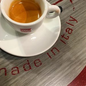 An espresso in a small cup and saucer on a table with the words "made in Italy" written on it.