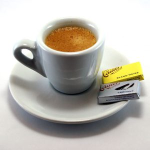 Espresso in a small cup and saucer with two tablets of chocolate resting on the saucer.