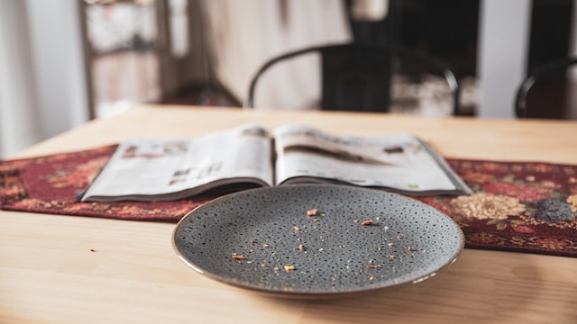 A wooden table with a dirty dark grey plate and an opened magazine
