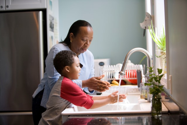 Person and child washing their hands in a kitchen sink