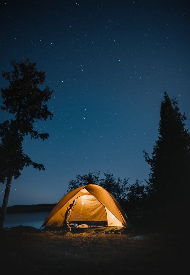 A tent in the woods with people inside and light on