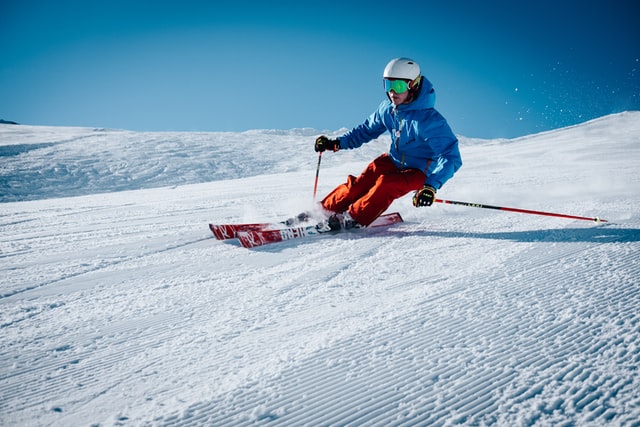 Man with blue jacket and red pants skiing on fresh snow