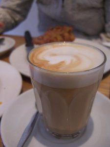 Coffee drink with milk in a clear glass on a saucer.