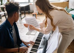 Piano teacher pointing to sheet music. Student at the piano watching.