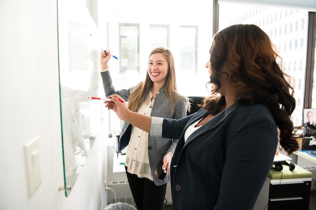 Two women writing on a white board