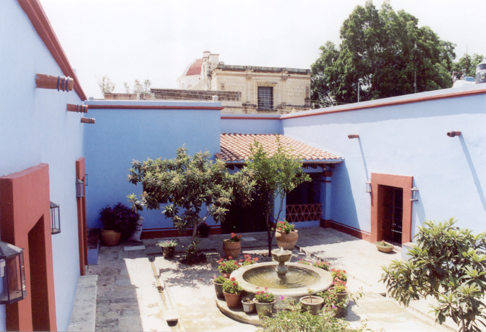 Courtyard with a fountain and plants, surrounded by a blue house with red brick details.