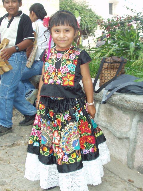 Young girl wearing black dress covered with colorful floral patterns, with a white lace hem