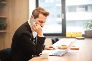 Business person on a phone call in front of a laptop and mug.