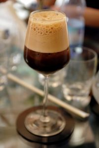 Foamy coffee drink in a clear, stemmed glass on a coaster